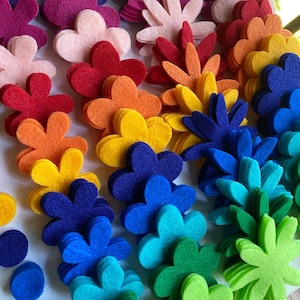 Può includere: Un assortimento arcobaleno di forme di fiori in feltro, impilate in file. I fiori sono in tonalità di viola, rosa, rosso, arancione, giallo, blu, verde e verde lime.