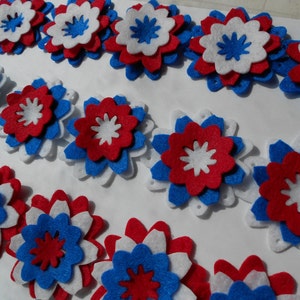May include: A collection of felt flowers in red, white, and blue. The flowers are layered and have a star-shaped center.