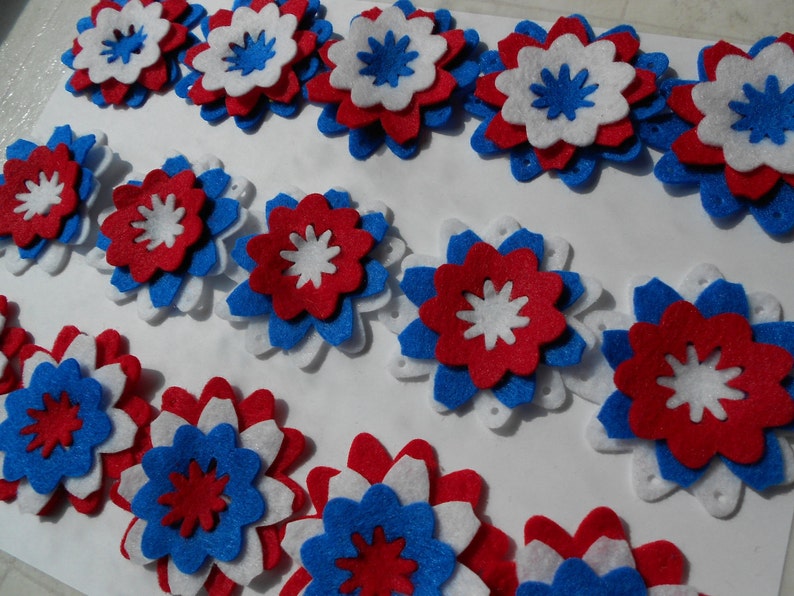 May include: A collection of felt flowers in red, white, and blue. The flowers are layered and have a star-shaped center.
