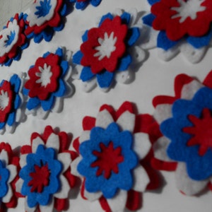 May include: A collection of felt flowers in red, white, and blue. The flowers are layered and have a starburst design.