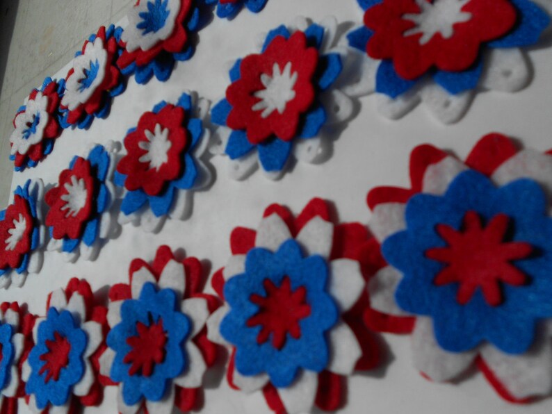 May include: A collection of felt flowers in red, white, and blue. The flowers are layered and have a starburst design.