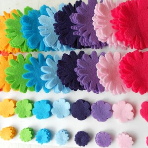 K&ouml;nnte beinhalten: Eine Regenbogen-Auswahl an Filzblumenformen in verschiedenen Gr&ouml;&szlig;en. Die Blumen sind in Reihen angeordnet, wobei die gr&ouml;&szlig;ten Blumen oben und die kleinsten Blumen unten sind.