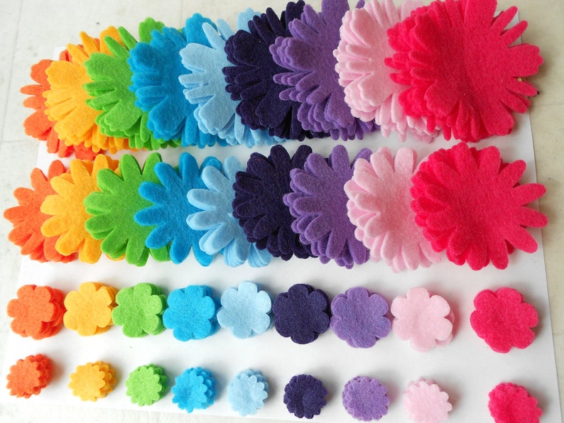 K&ouml;nnte beinhalten: Eine Regenbogen-Auswahl an Filzblumenformen in verschiedenen Gr&ouml;&szlig;en. Die Blumen sind in Reihen angeordnet, wobei die gr&ouml;&szlig;ten Blumen oben und die kleinsten Blumen unten sind.