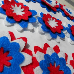 May include: A collection of felt flowers in red, white, and blue. The flowers are layered and have a starburst design.
