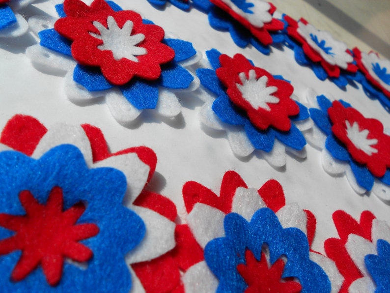 May include: A collection of felt flowers in red, white, and blue. The flowers are layered and have a starburst design.
