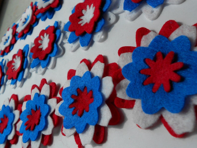 May include: A collection of felt flowers in red, white, and blue. The flowers are layered and have a starburst design in the center.