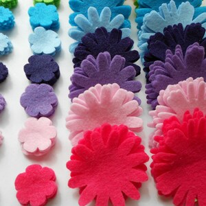 K&ouml;nnte beinhalten: Sortiment an Filzblumenformen in verschiedenen Farben, darunter Gr&uuml;n, Blau, Lila, Rosa und Rot. Die Blumen sind in Stapeln &uuml;bereinander gelegt und erzeugen einen Farbverlaufseffekt.