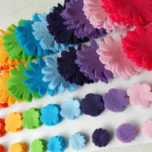 K&ouml;nnte beinhalten: Eine Regenbogen-Auswahl an Filzblumenformen, in Reihen gestapelt. Die Blumen sind in verschiedenen Gr&ouml;&szlig;en und Farben, darunter Rot, Rosa, Lila, Blau, Gr&uuml;n und Orange.