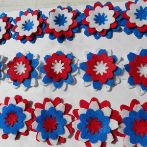 May include: A collection of felt flowers in red, white, and blue. The flowers are layered and have a star-shaped center.