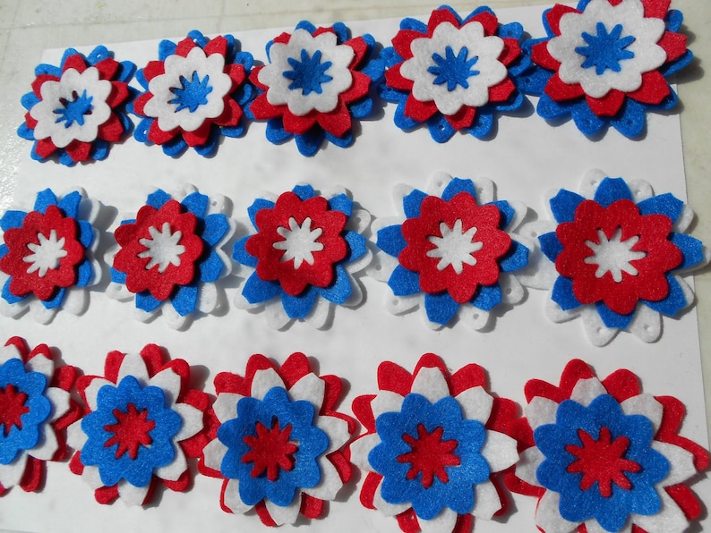 May include: A collection of felt flowers in red, white, and blue. The flowers are layered and have a star-shaped center.