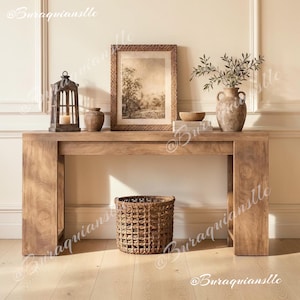May include: A wooden console table holds a dark metal lantern with a candle, a small brown vase, a framed landscape print, a wooden bowl, and a textured ceramic jug with leafy branches. A woven basket sits on the floor beneath the table.