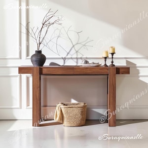May include: A rectangular wooden console table with a smooth finish and two drawers. On top sits a dark textured vase with bare branches, a small white dish with pinecones, and two pillar candles on dark metal stands. A woven basket sits below.