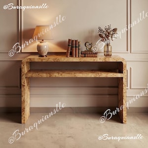 May include: A burl wood console table with a curved waterfall design and a lower shelf. On top sits a table lamp with a beige shade, a stack of four vintage books, a small gold-toned abstract sculpture, and a glass vase with dried flowers.