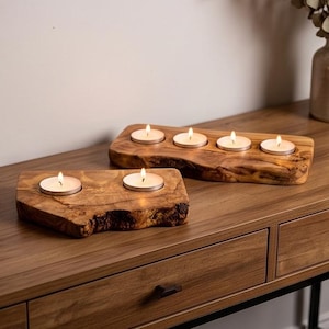 May include: Two natural wood candle holders with live edges, one holding two lit tea light candles and the other holding four lit tea light candles. The wood features a light brown grain with dark knots and a smooth, polished finish on top.