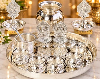 Può includere: Un set puja thali in metallo color argento composto da un grande vassoio rotondo, un vaso centrale, due lampade a olio decorate con figure di divinità, quattro ciotole con base testurizzata, un cucchiaino, un campanello e un porta incenso lucido.