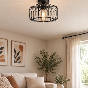 Pode incluir: Uma luminária de teto embutida na cor preto fosco com um design de gaiola cilíndrica feita de barras de metal finas. A luminária contém uma única lâmpada exposta estilo Edison que emite um brilho quente, projetando sombras suaves no teto.