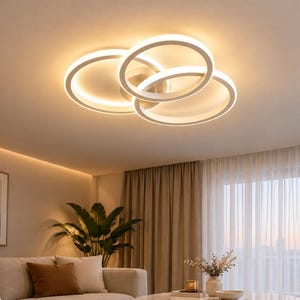 Pode incluir: Uma luminária de teto com três anéis circulares brancos sobrepostos que emitem um brilho quente e difuso. A estrutura é montada rente ao teto, criando um design geométrico em camadas que ilumina o ambiente abaixo.