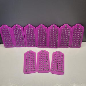 Peut inclure: Un ensemble de dix plaques de multiplication violettes en forme de pierre tombale, numérotées de un à dix en haut. Chaque plaque affiche une série complète d'équations de multiplication de un à dix, avec des chiffres et du texte argentés en relief.