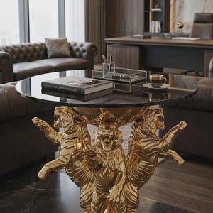 May include: A round table with a black glass top supported by a gold-colored base featuring three sculpted tigers standing on their hind legs. The tigers are depicted with open mouths and detailed fur textures, resting on a circular gold pedestal.