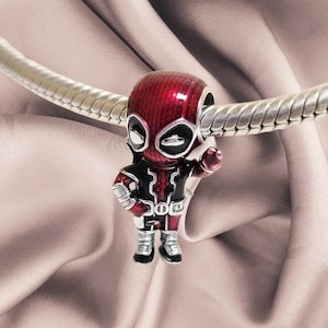 May include: A silver-toned metal charm bead shaped like a stylised character with a red and black enamelled suit, white eye patches, and a raised hand, threaded onto a flexible silver-toned snake chain bracelet with a textured, segmented design.