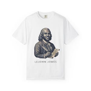 May include: A white short-sleeve t-shirt featuring a dark-toned graphic illustration of a person in 18th-century attire holding a quill and parchment. The text "76ers" is on the scroll, and the name "LEJAWN JAMES" is printed below the graphic.