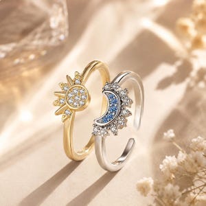 Peut inclure: Deux bagues ouvertes aux motifs célestes. Une bague dorée présente un design de soleil avec des pierres pavées transparentes. La seconde bague argentée arbore une forme de croissant de lune ornée de pierres bleues et d'étoiles pavées.