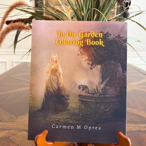 May include: A softcover coloring book titled In the Garden Coloring Book by Carmen M Oprea. The cover features an illustration of a person in a long dress holding a bucket near a stone fountain with a cat, set against a dark, atmospheric background.