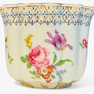 Puede incluir: Una maceta de porcelana de color crema con borde festoneado y un patrón de celosía pintado en oro con detalles azules. El exterior está decorado con arreglos florales pintados a mano que incluyen una gran rosa rosa y un tulipán morado.