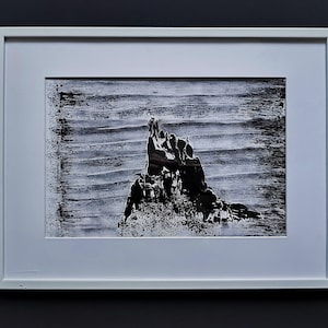 Puede incluir: Una impresión abstracta en blanco y negro enmarcada que presenta una forma central dentada similar a una montaña sobre un fondo texturizado con líneas horizontales. La obra está en un marco rectangular blanco simple con un borde de paspartú.