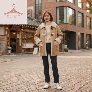 May include: A tan suede toggle coat with a cream-coloured faux shearling lining, collar, and cuffs. The coat features two front patch pockets and wooden toggle closures. It is worn over a cream turtleneck jumper and dark grey denim jeans.