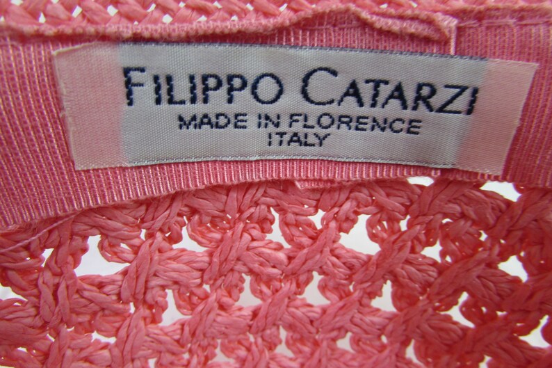 May include: A pink woven hat with a white label that reads "Filippo Catarzi Made in Florence Italy".