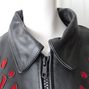 May include: Black leather jacket with a red floral design. The jacket has a zipper closure and a collar.