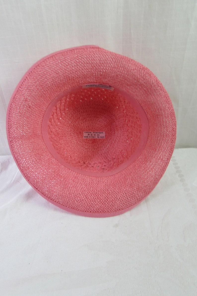May include: Pink straw hat with a woven texture. The hat has a label inside that reads "100% Paper, Size 57, Made in Italy".