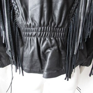 May include: Black leather jacket with fringe detailing. The jacket has a cinched waist and a zipper closure.