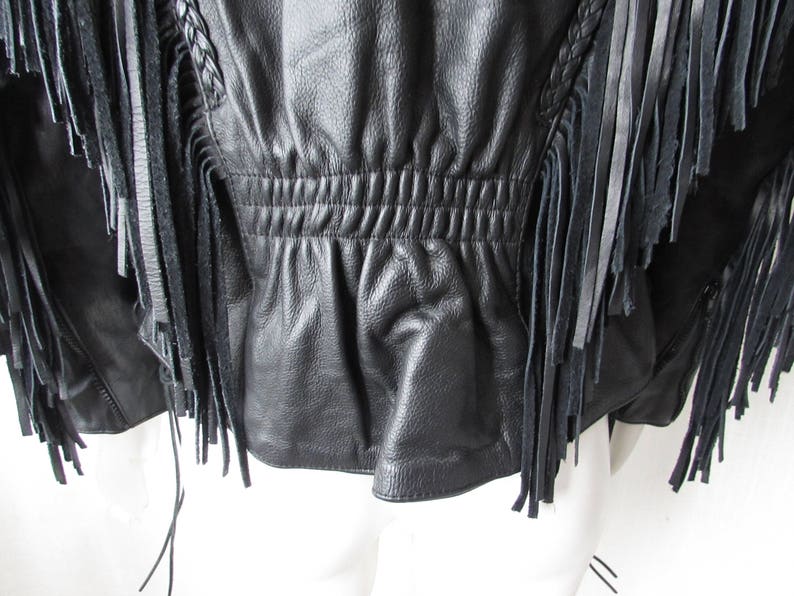 May include: Black leather jacket with fringe detailing. The jacket has a cinched waist and a zipper closure.