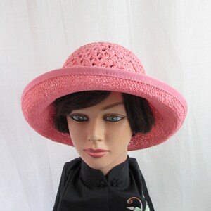 May include: A pink crocheted sun hat with a wide brim. The hat is made of a soft, lightweight material and has a simple, elegant design.