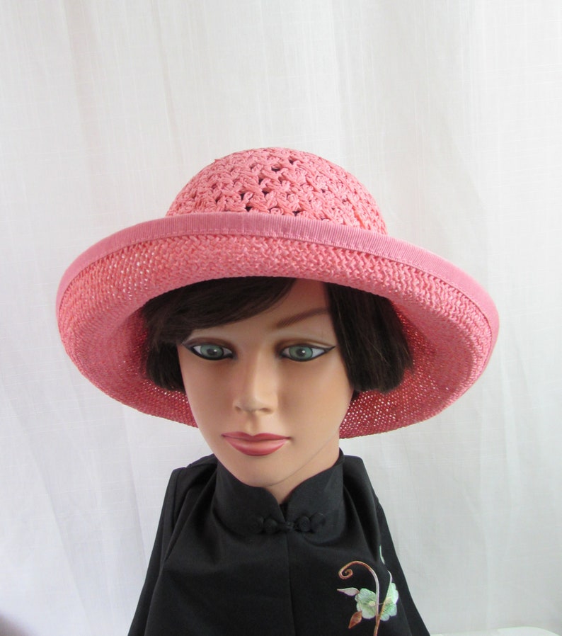 May include: A pink crocheted sun hat with a wide brim. The hat is made of a soft, lightweight material and has a simple, elegant design.