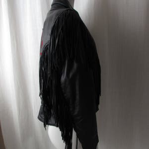May include: Black leather jacket with fringe detailing. The jacket has a zipper closure and a stand-up collar.