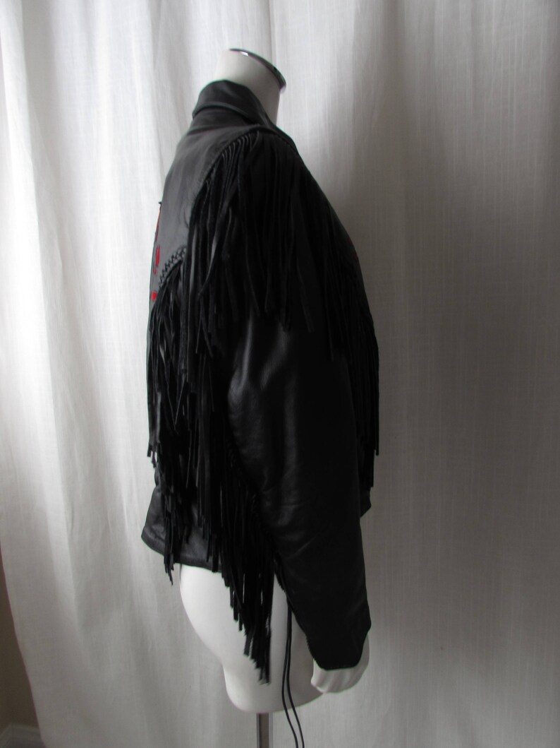 May include: Black leather jacket with fringe detailing. The jacket has a zipper closure and a stand-up collar.