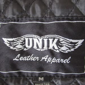 May include: Black leather apparel label with white stitching. The label features a white winged logo with the text "UNIK Leather Apparel" in white.
