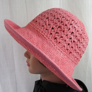 May include: A pink crocheted sun hat with a wide brim. The hat is made of a lightweight material and has a delicate, open weave.