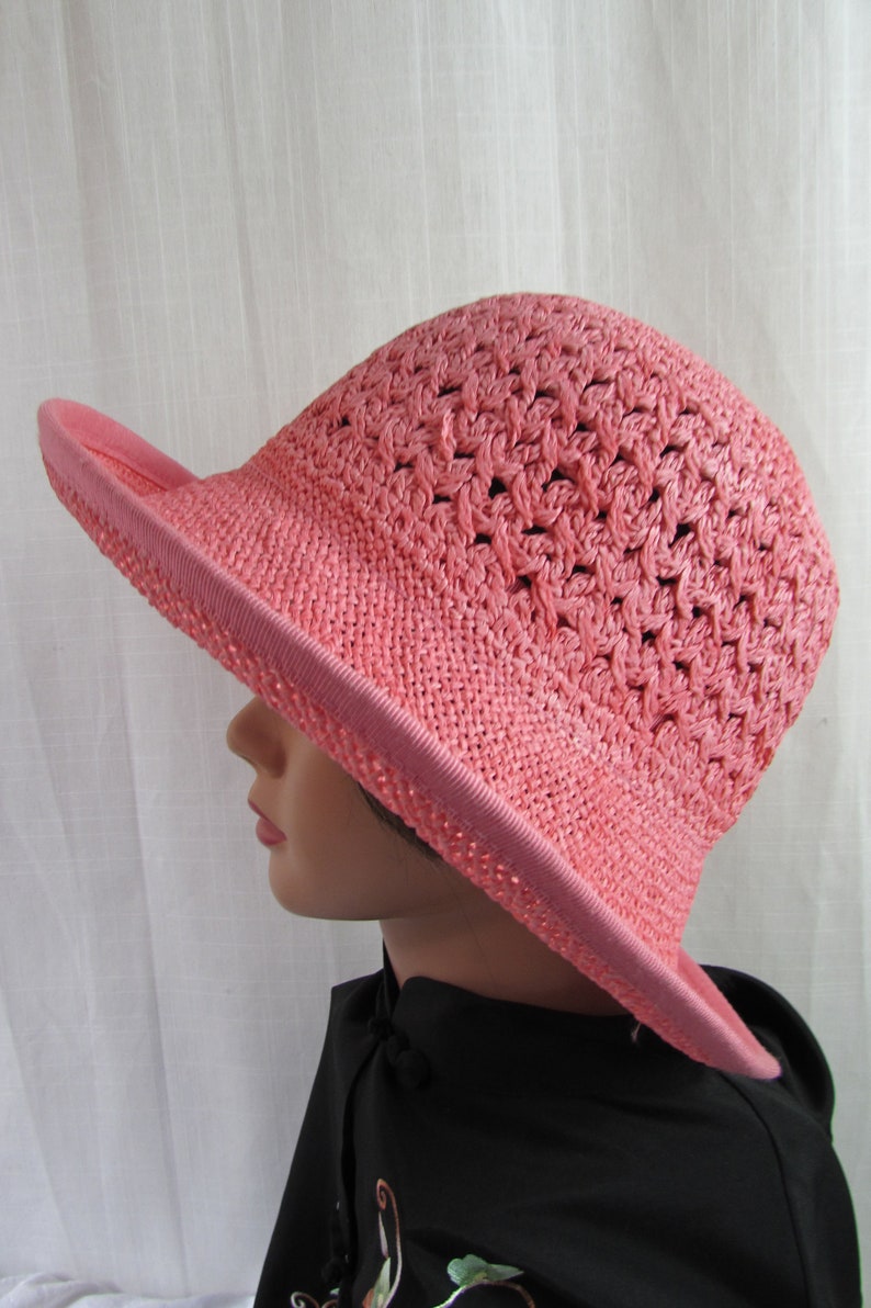 May include: A pink crocheted sun hat with a wide brim. The hat is made of a lightweight material and has a delicate, open weave.