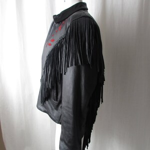May include: Black leather jacket with fringe detailing and red embroidery. The jacket has a zipper closure and long sleeves.