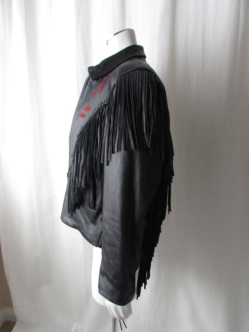 May include: Black leather jacket with fringe detailing and red embroidery. The jacket has a zipper closure and long sleeves.