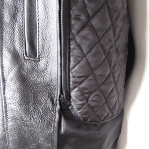 May include: Close-up of a black leather jacket with a quilted lining. The jacket has a zipper closure and a pocket on the left side.