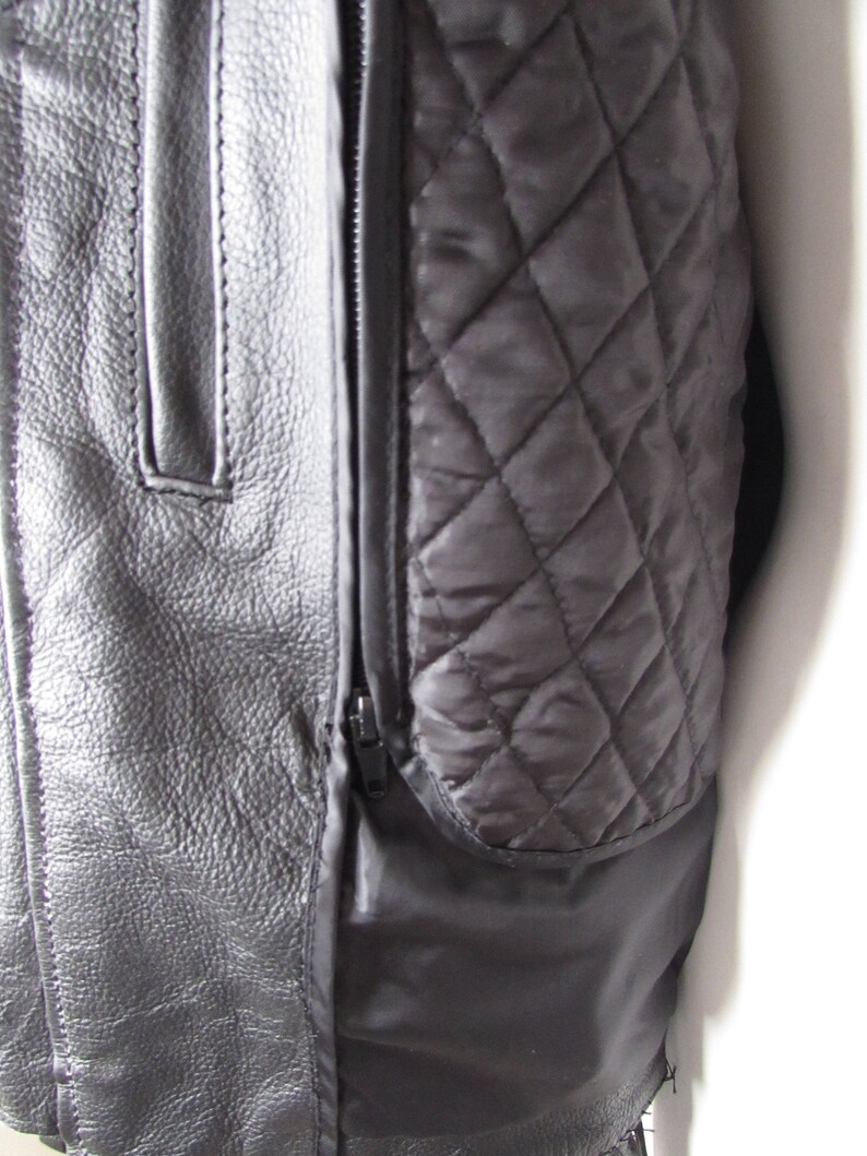 May include: Close-up of a black leather jacket with a quilted lining. The jacket has a zipper closure and a pocket on the left side.