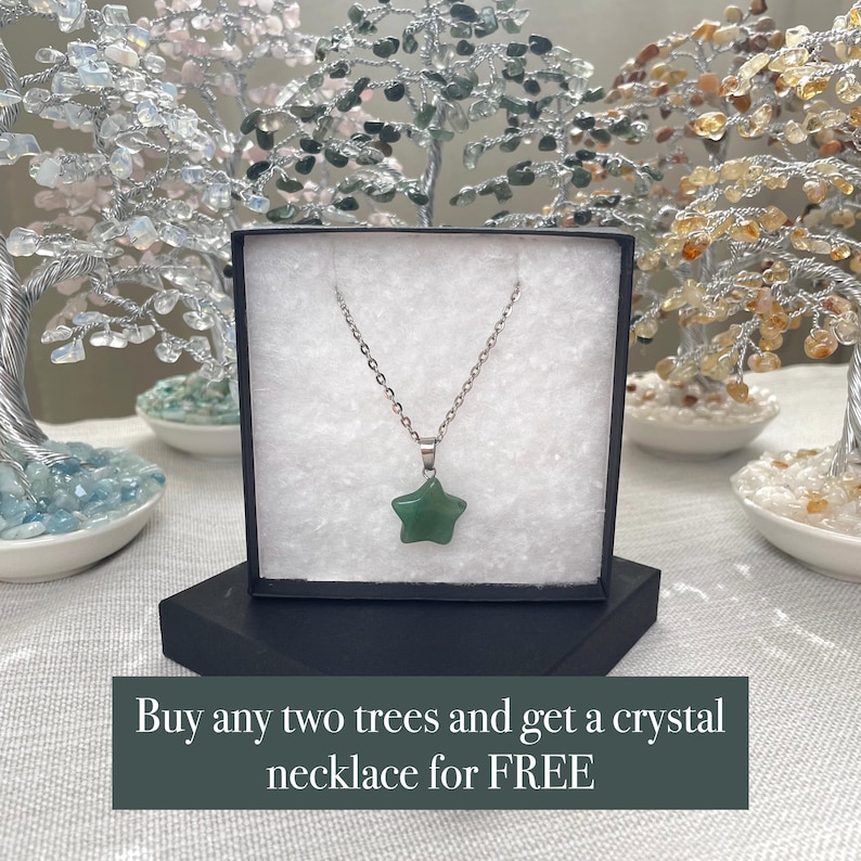 May include: A silver-toned metal chain necklace featuring a green star-shaped gemstone pendant, displayed inside a black gift box with white padding. The box includes the text: Buy any two trees and get a crystal necklace for FREE.