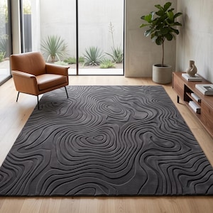May include: A large rectangular area rug in a dark charcoal gray color featuring a raised, three-dimensional topographic map pattern of concentric, flowing, and irregular lines that create a textured surface across the entire floor covering.