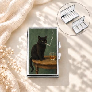 Peut inclure: Un étui à cigarettes rectangulaire en métal orné d'une illustration imprimée représentant un chat noir assis sur une table en bois avec un verre de liquide ambré et une cigarette allumée. L'étui possède un cadre argenté et un couvercle articulé.