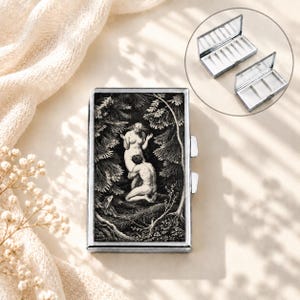 Peut inclure: Un pilulier rectangulaire en métal avec une illustration en noir et blanc de deux personnages dans une forêt sur le couvercle. Le boîtier possède un cadre argenté et un fermoir à bouton-poussoir. L'intérieur est divisé en trois compartiments blancs.